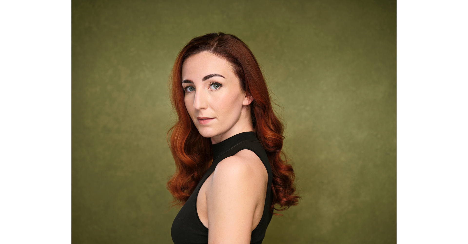actress  black top with red hair standing front of a green painted canvas backdrop